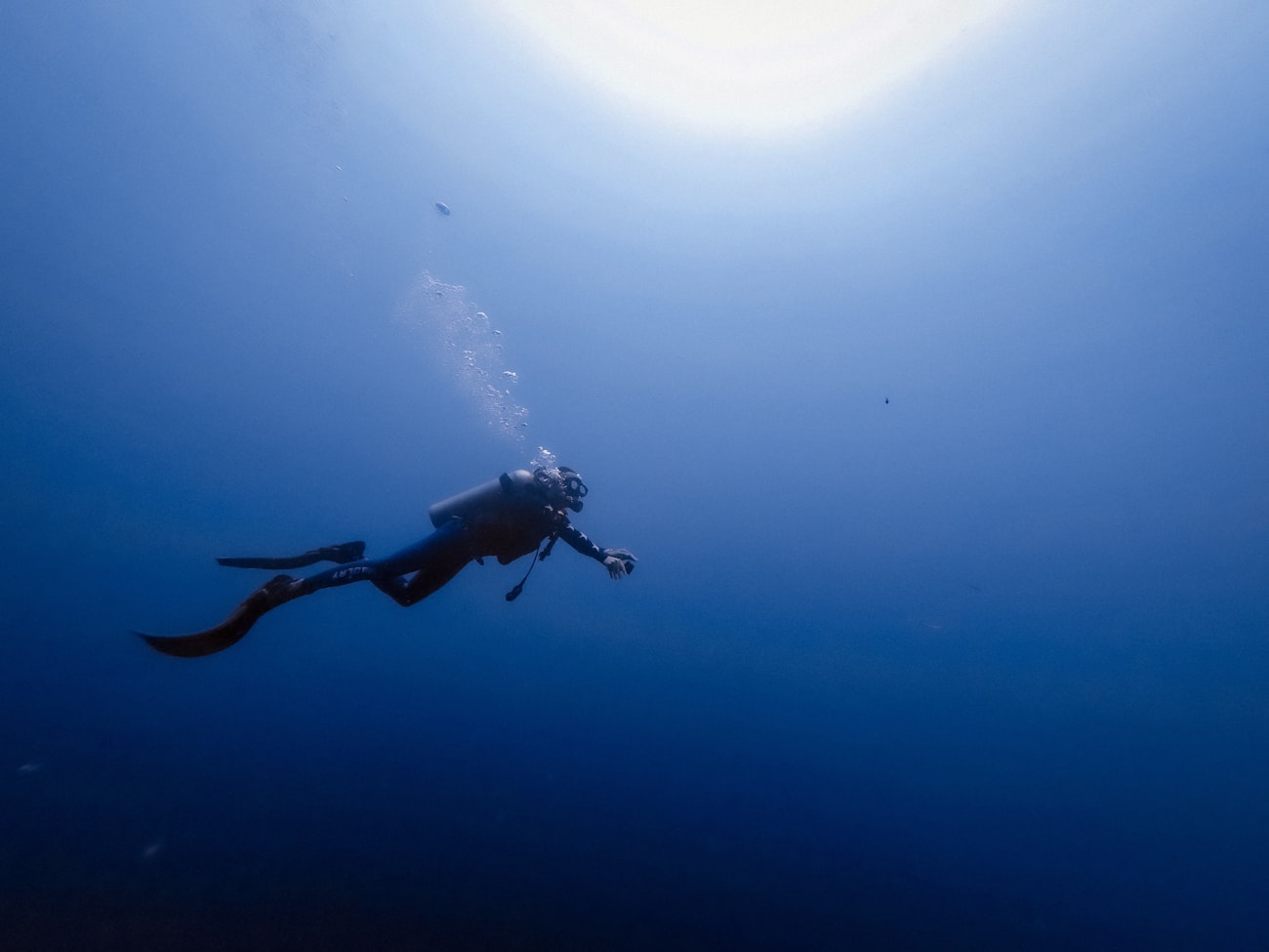 Lone scuba diver silhouetted in deep blue water, bubbles rising towards the sunlit surface