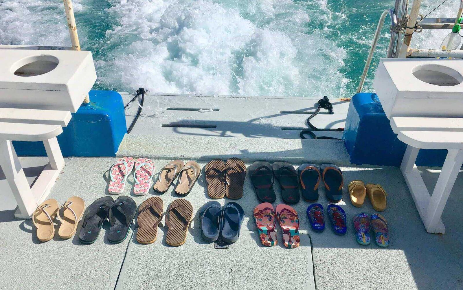 Fourteen pairs of flip-flops lined up on the boat's stern deck, the wake churning white behind them