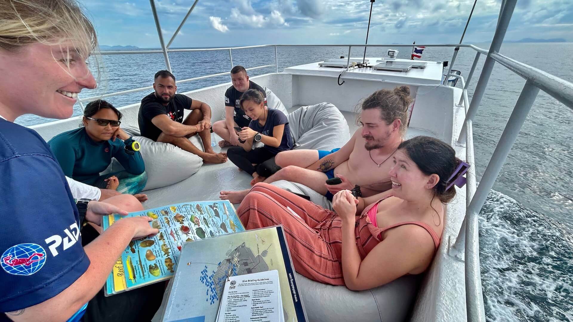 Aloha Diving crew member briefing divers on the back deck of the dive boat, reef ID slate and dive briefing board in hand, Phuket