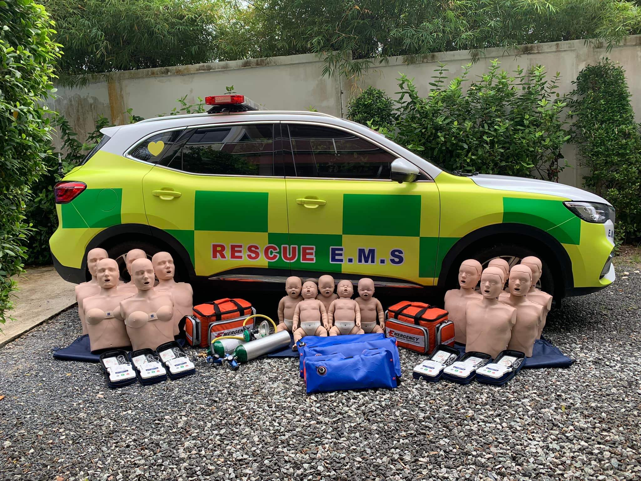 CPR manikins, AED trainers and oxygen kit laid out beside a Rescue EMS response car