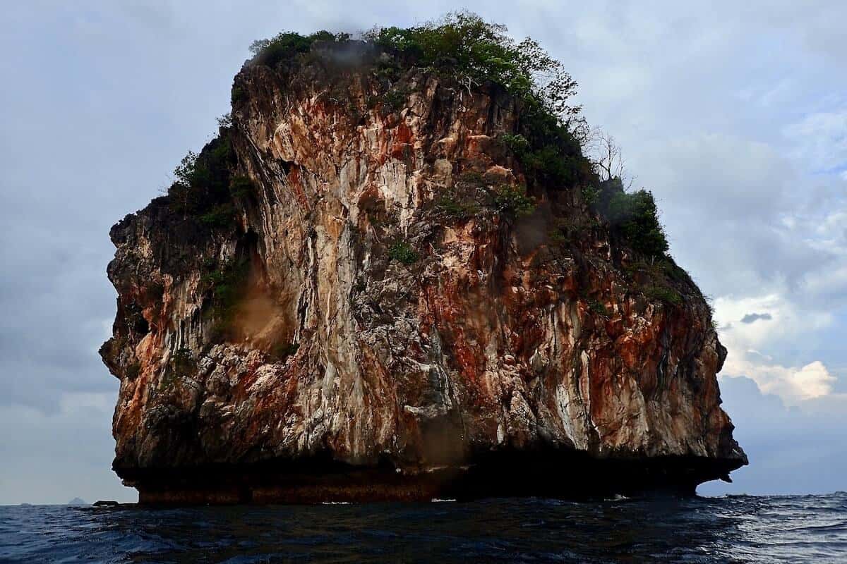 Steep limestone islet topped with green scrub rising sheer out of a calm sea