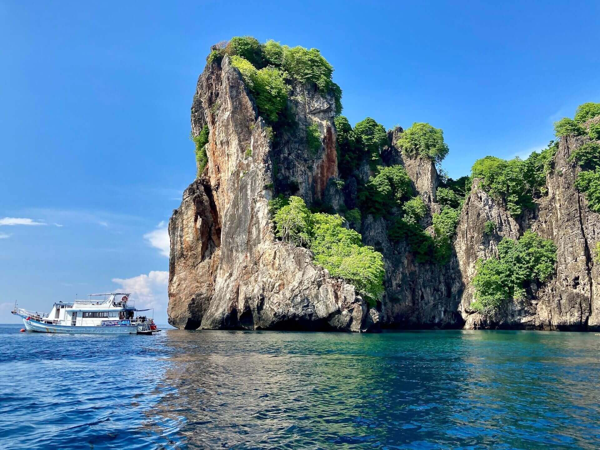 White two-deck dive boat moored beside a towering limestone cliff in turquoise water