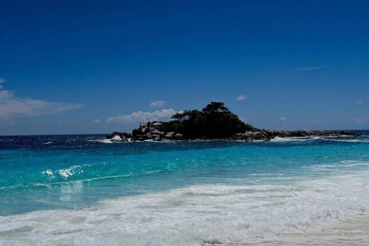 Turquoise surf breaking in the foreground with a small tree-topped rocky islet offshore