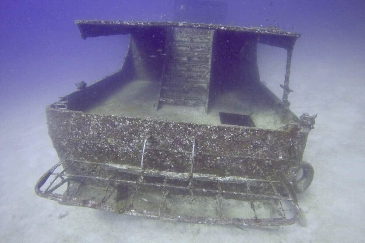 Encrusted small boat wreck upright on white sand, canopy roof and tyre fender intact