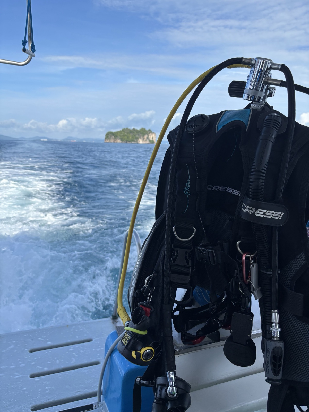 Rental buoyancy jacket and regulator hanging ready on the boat rail, wake and a small island astern