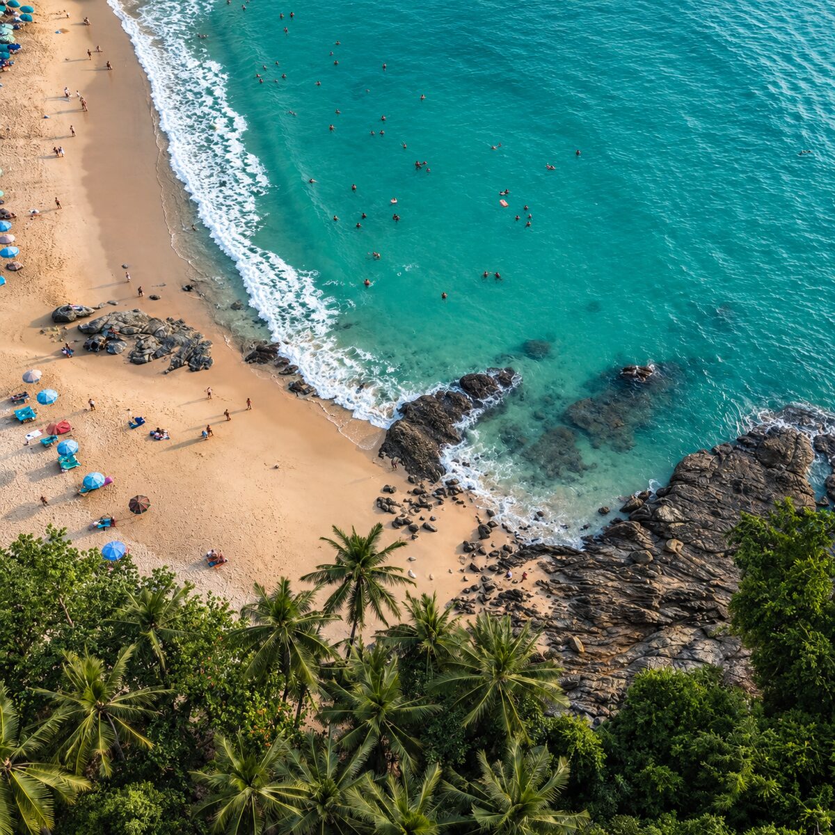 Surin Beach from above: a curve of pale sand between rocks and palms, swimmers in turquoise water