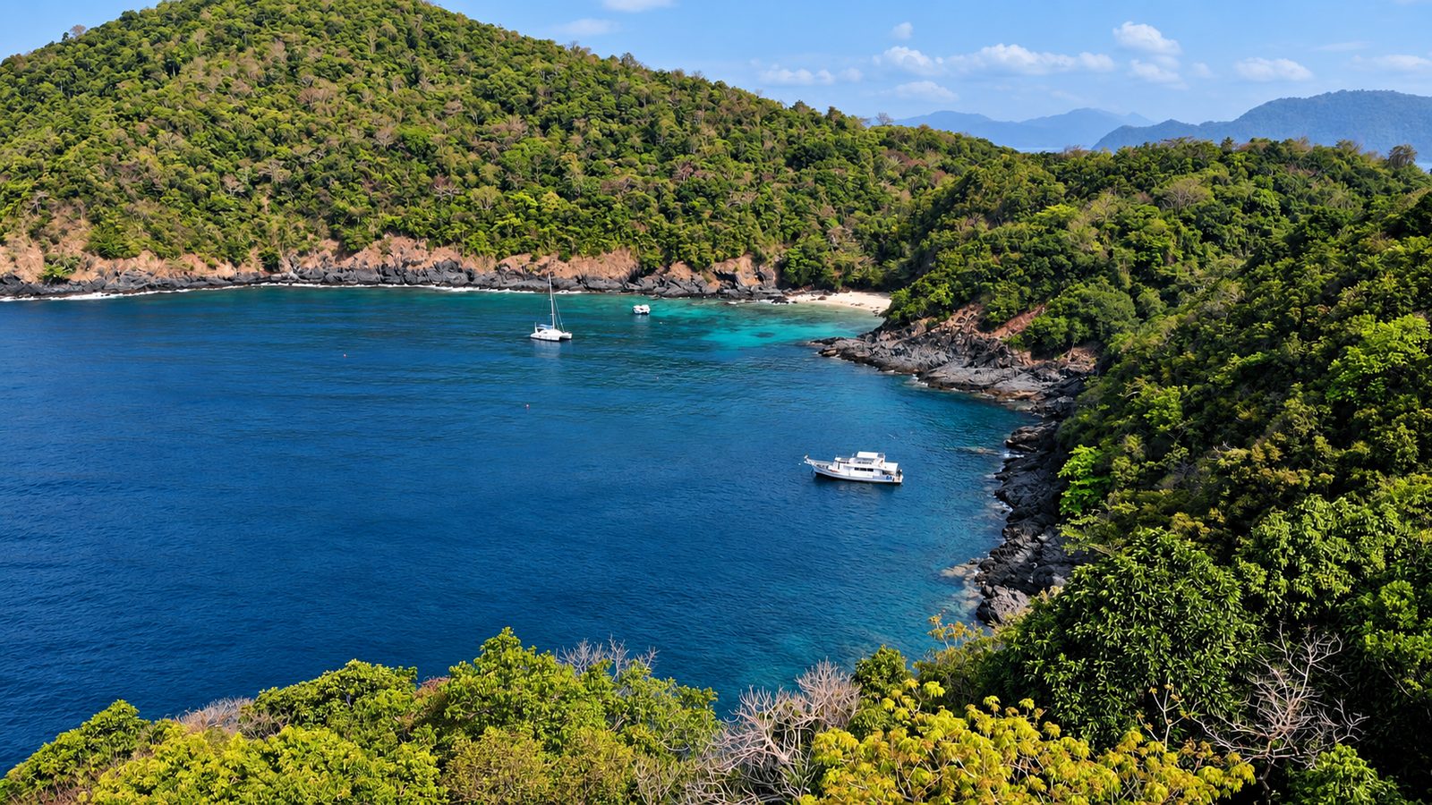 Windmill Bay from above: forested headlands, deep blue water and MV Matchanu at anchor