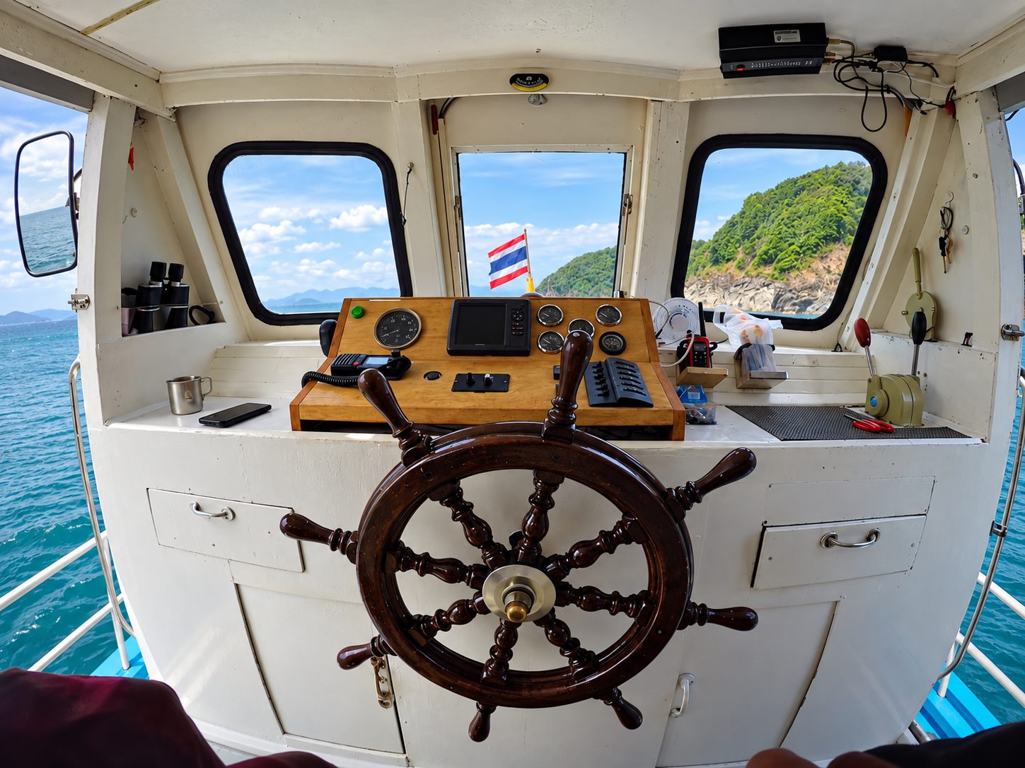 The wheelhouse: a wooden ship’s wheel and the instruments, a green island through the windows