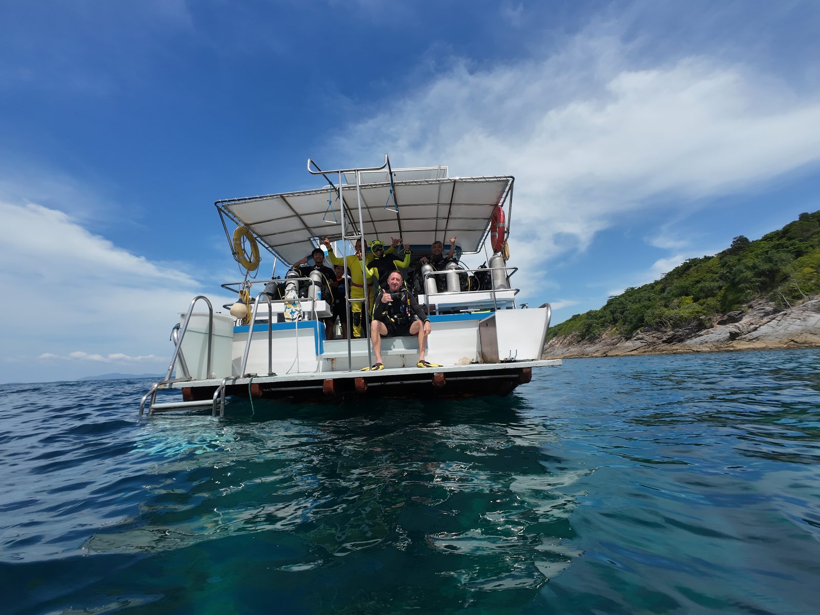 Divers kitting up at the stern, the swim deck down, a rocky island behind