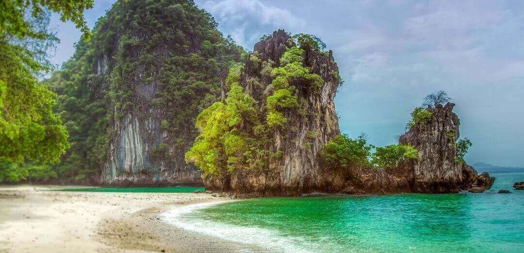 Empty white-sand beach curving past jungle-topped limestone karsts into clear turquoise shallows