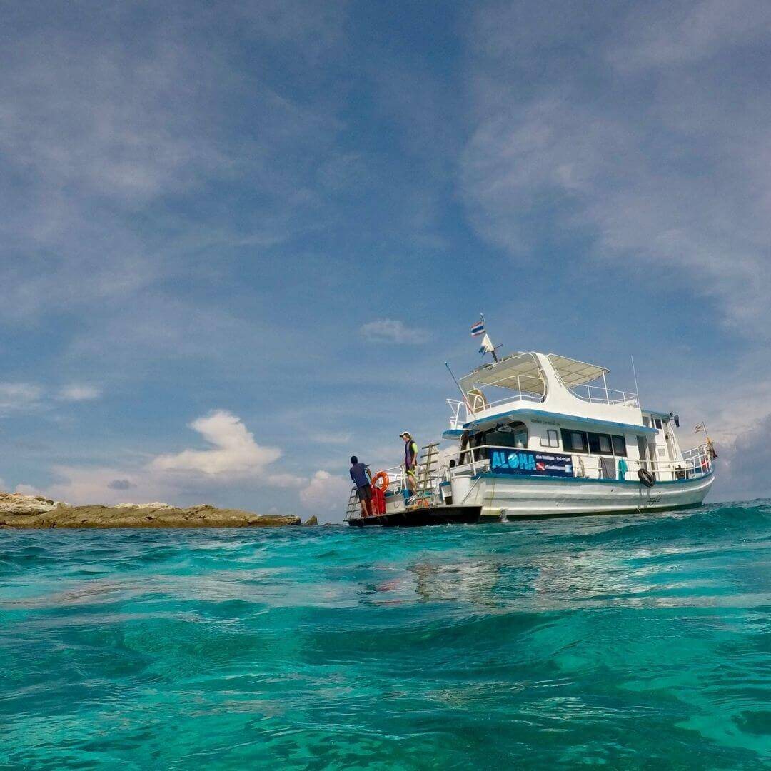 Aloha dive boat moored off a rocky islet with two people on its rear platform