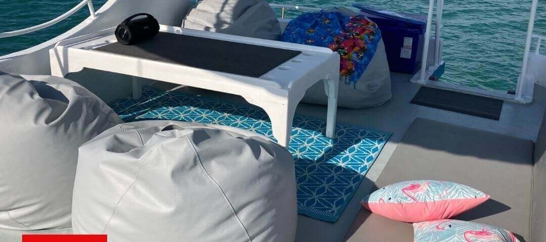 Boat sun deck laid out with grey beanbags, flamingo cushions and a low white table