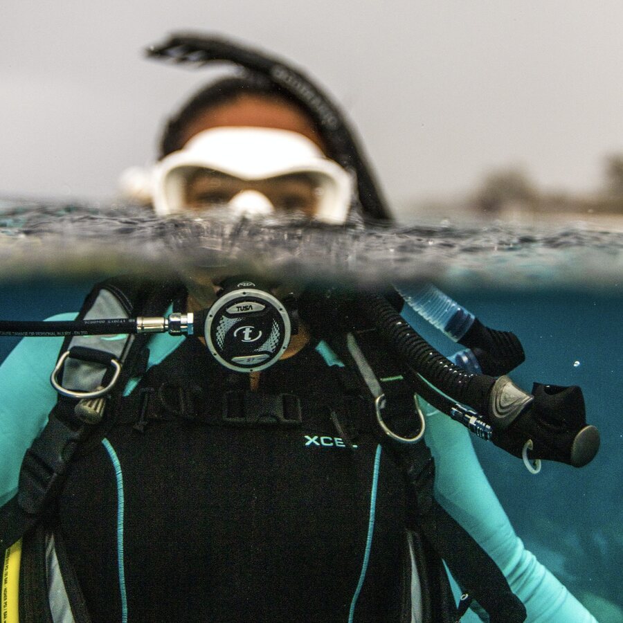 A divemaster at the surface in a split shot, regulator and gauges hanging from the BCD (PADI)
