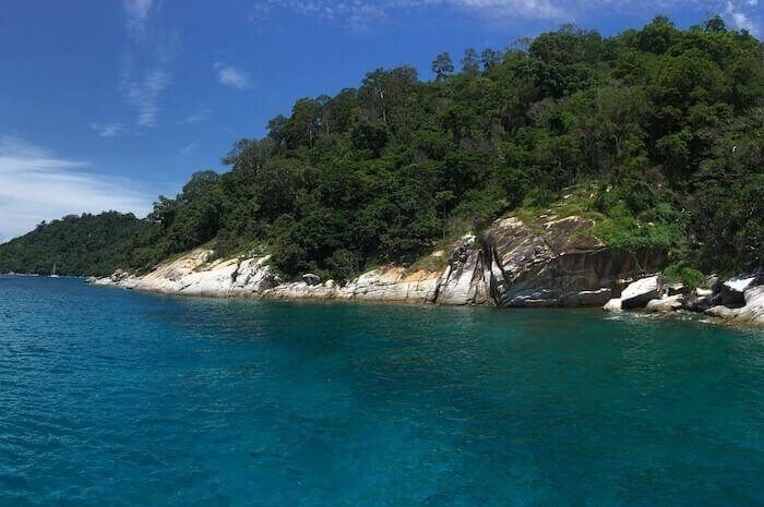A small green island with a rocky shore in flat blue water