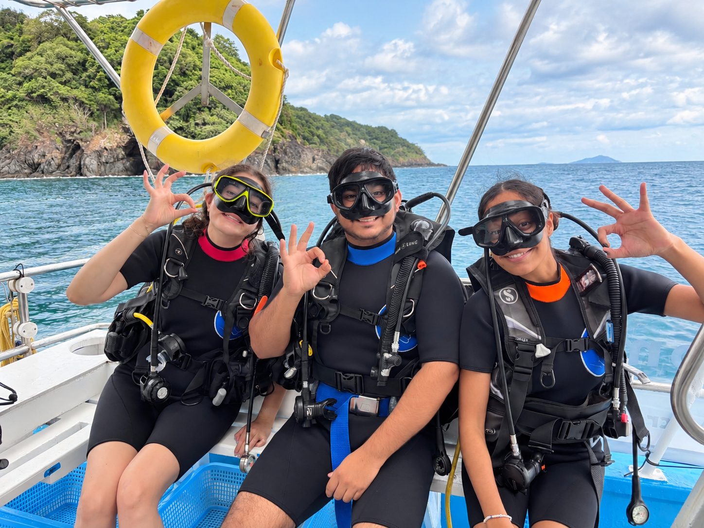 Three guests in dive gear on the bench, all giving the OK sign