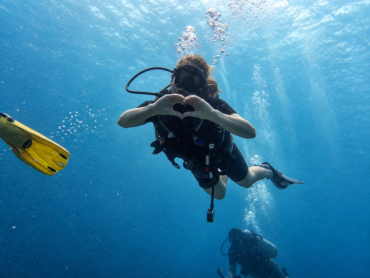 Two divers in the blue, one signalling OK, sunlight above