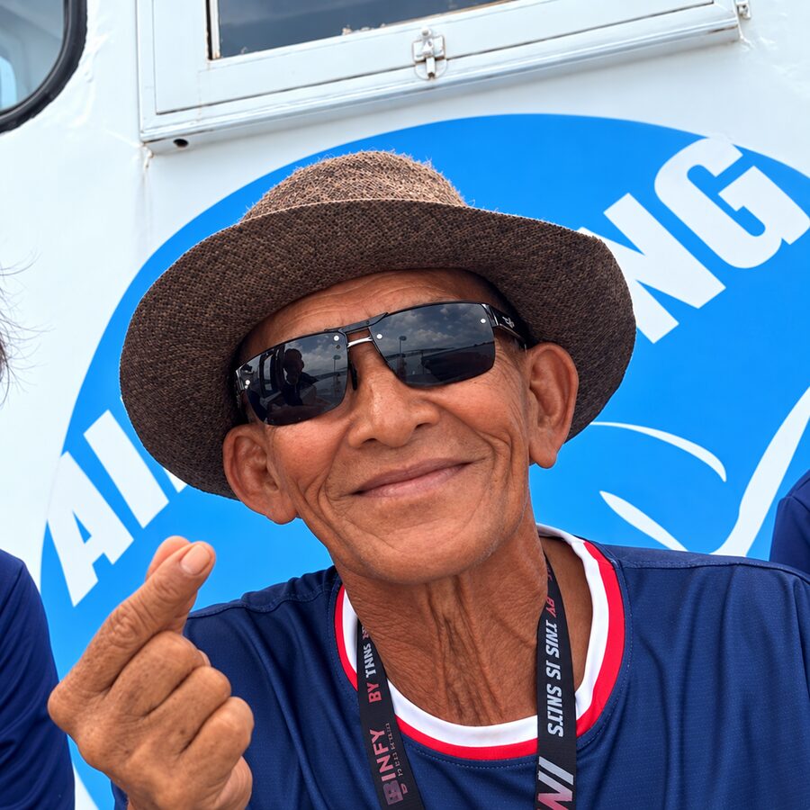Captain Lek in a straw hat and sunglasses, making a finger heart in front of the boat's Aloha Diving logo
