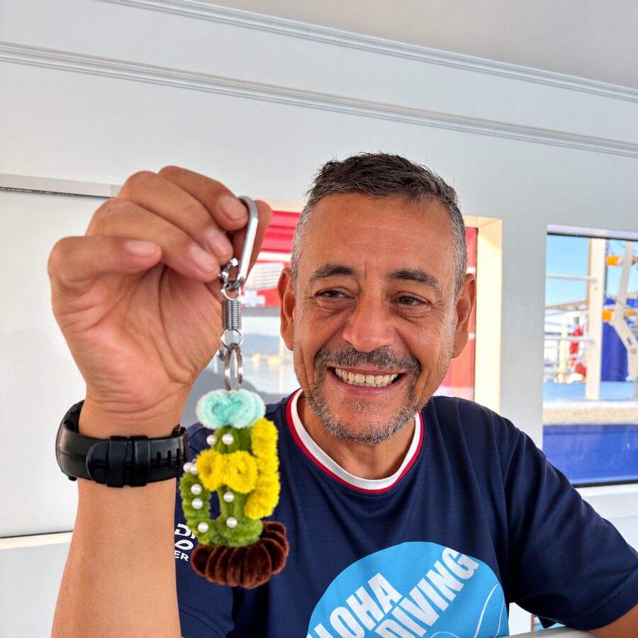 Günter at the boat's table, holding up a crocheted keyring and smiling
