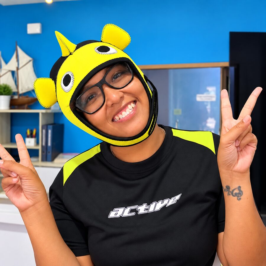 Mona in a yellow fish-shaped neoprene hood, grinning with two peace signs