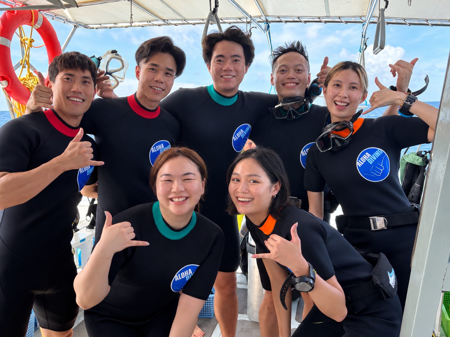 A group of young divers in Aloha wetsuits throwing shakas on deck