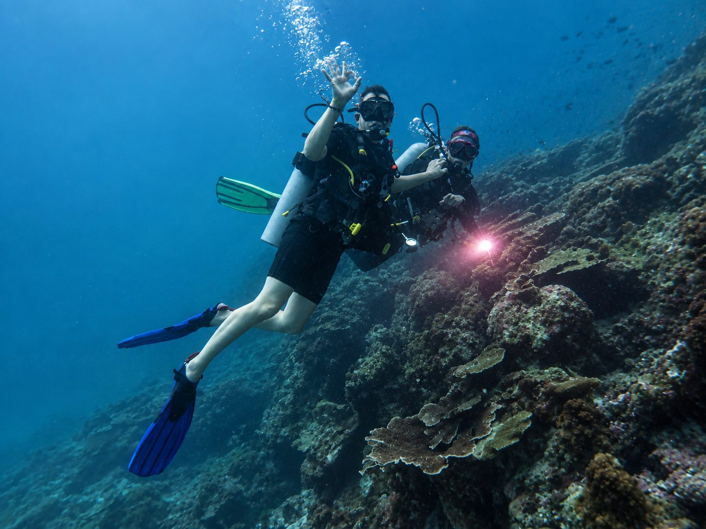Two divers on a coral-covered slope at Koh Doc Mai, one waving