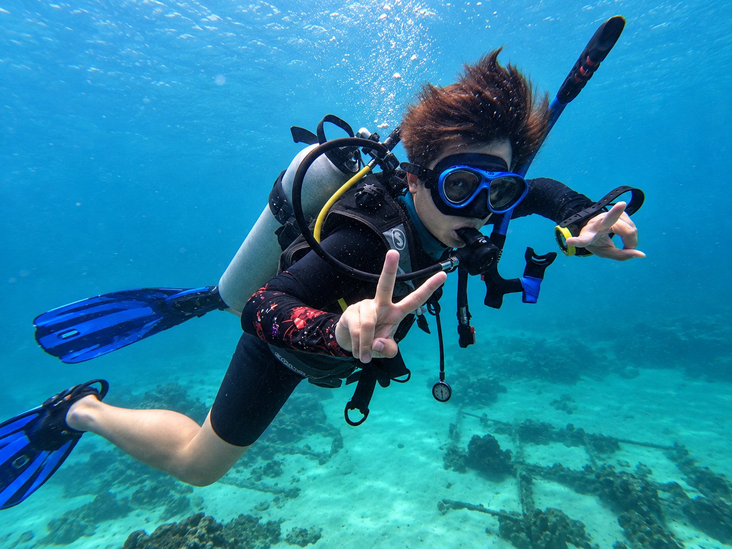 A diver making a peace sign over the sandy seabed at Koh Mai Thon