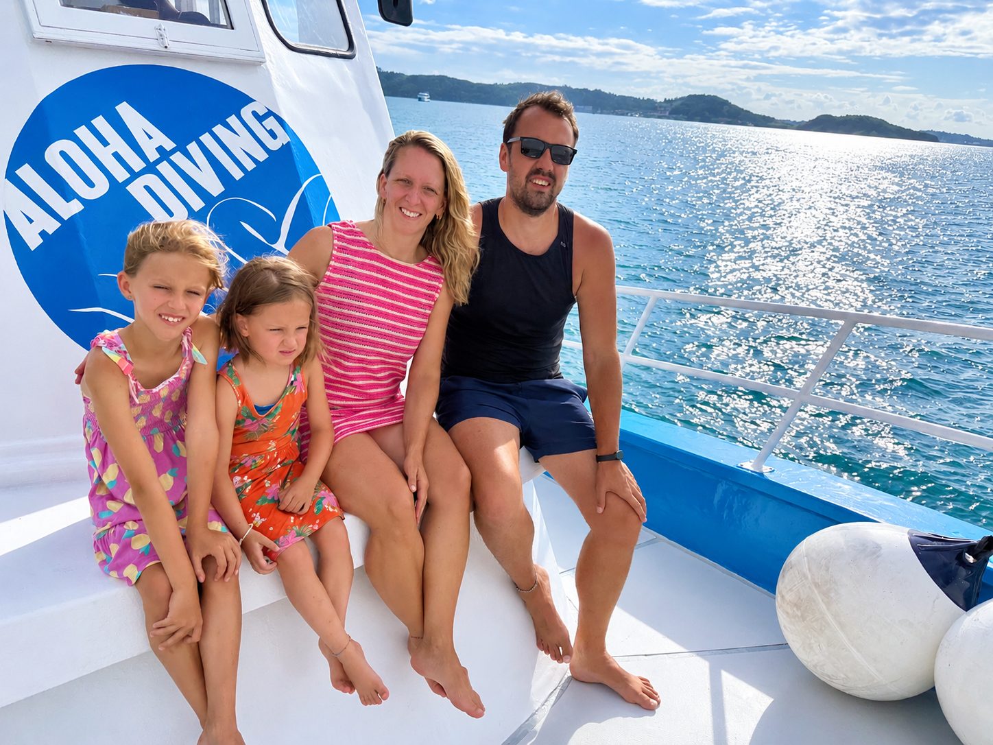 A family on the bow bench in front of the Aloha Diving flag