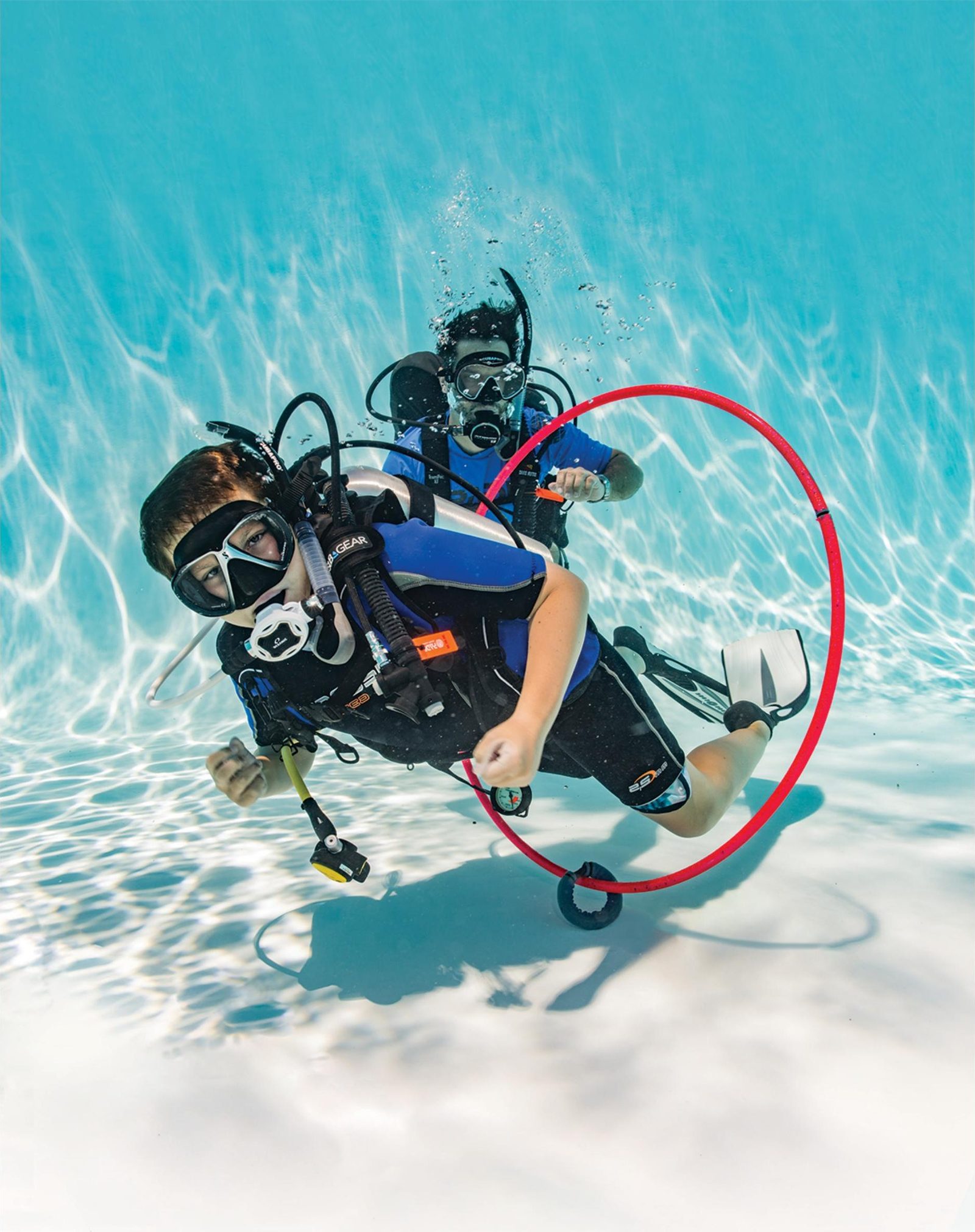 A young diver swimming through a hoop on the pool floor