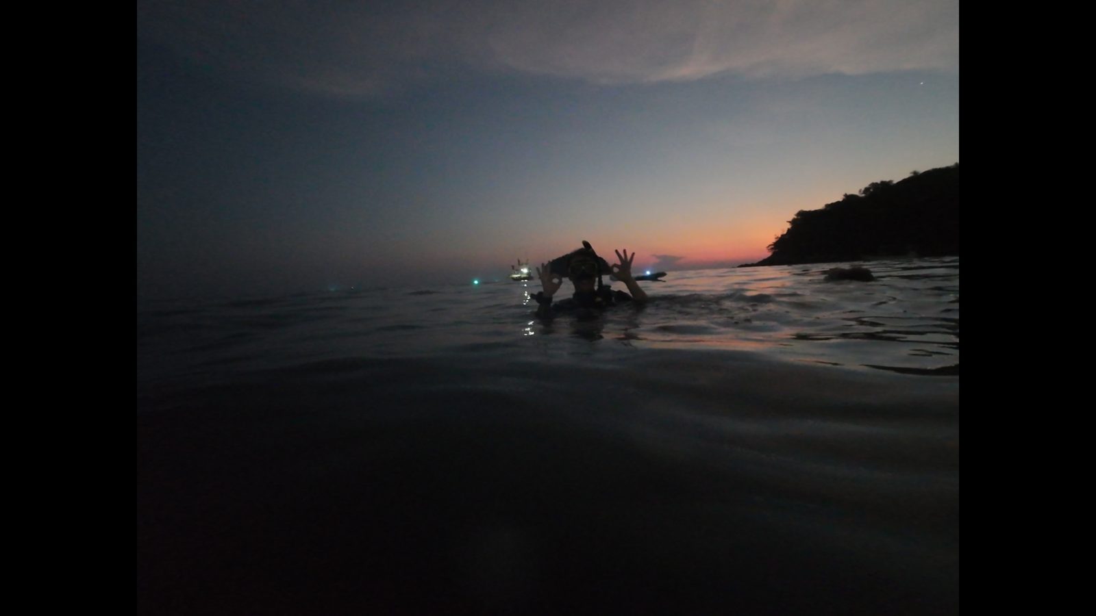 A diver in the shallows at dusk with the shore behind