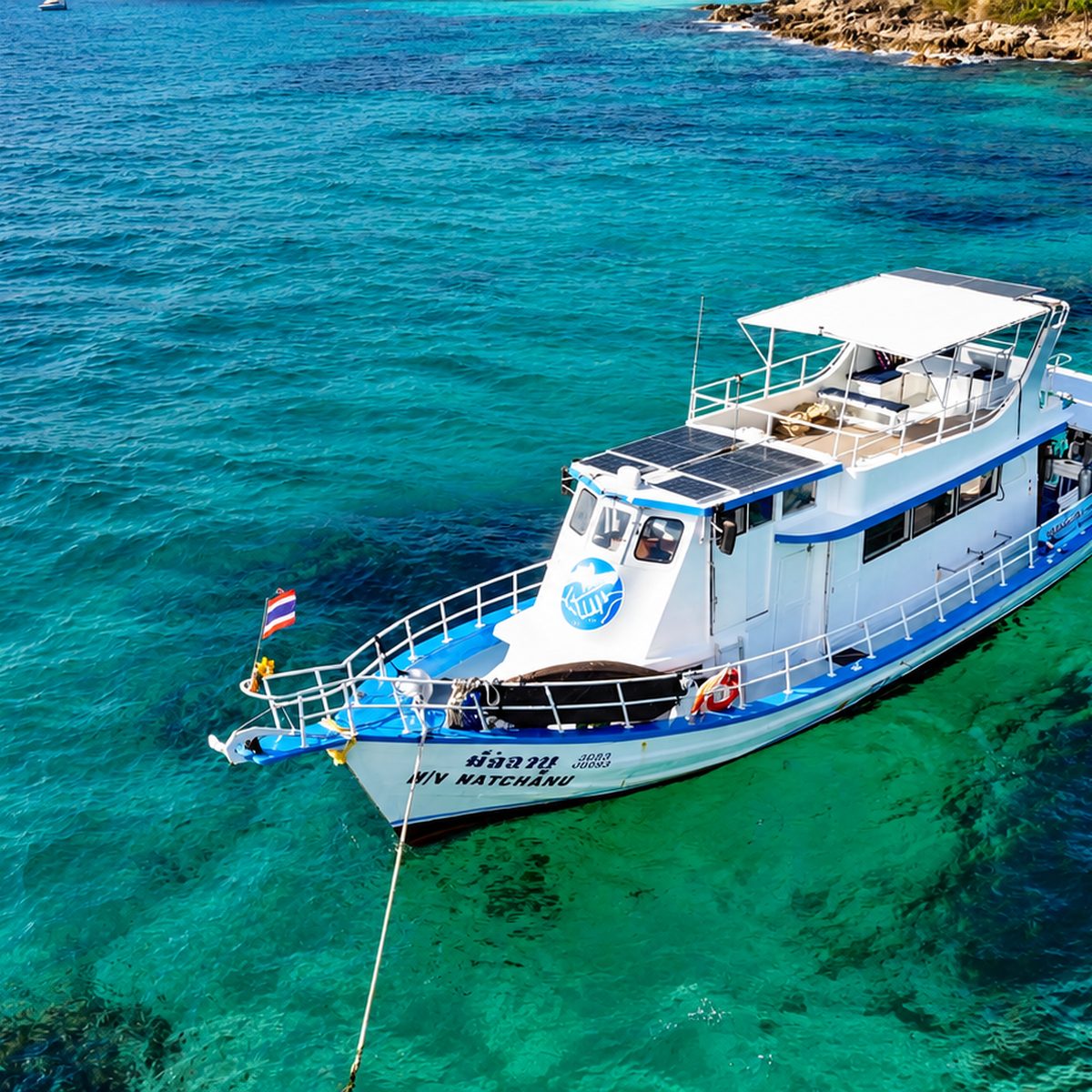 MV Matchanu at anchor in turquoise water, a forested island behind