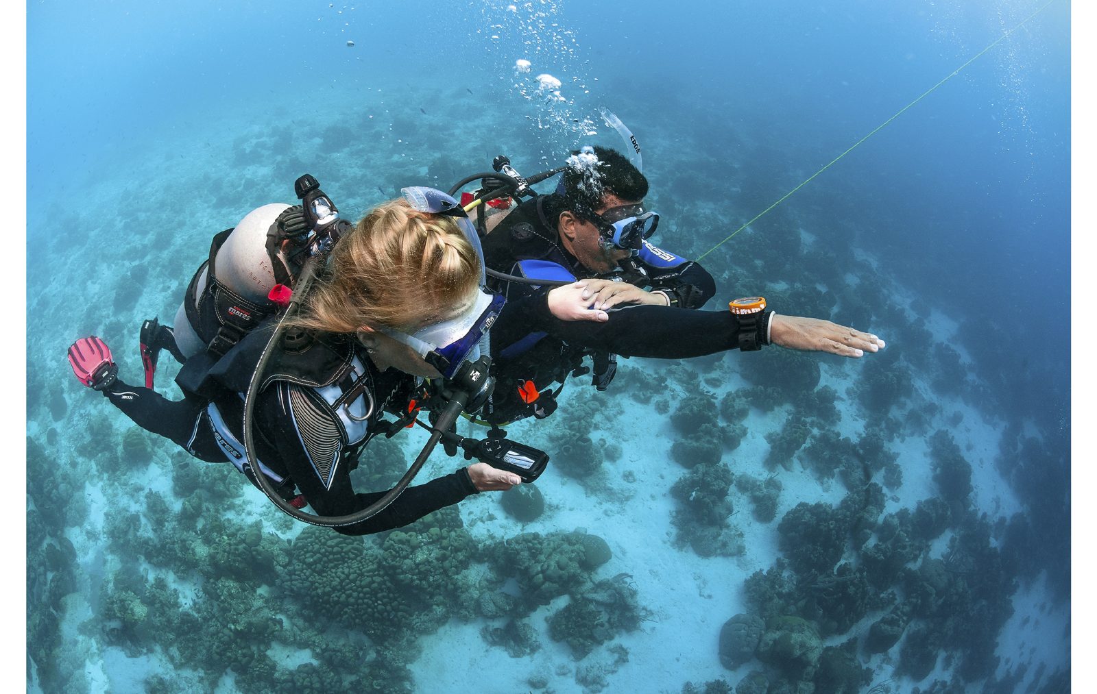 An instructor and a student hovering above a reef, sunlight on the water (PADI)