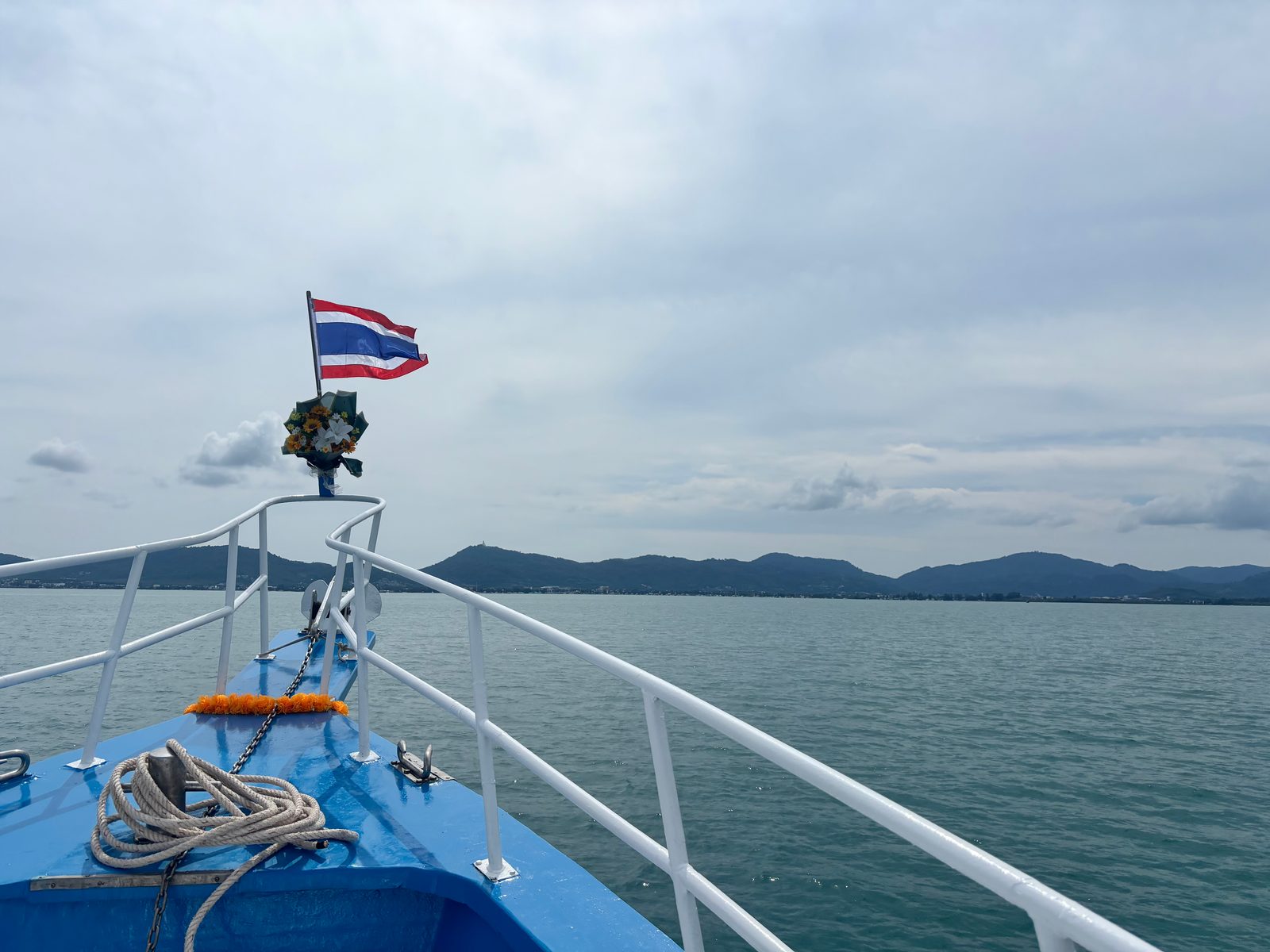 Heading back to Chalong: the bow, the Thai flag and the garland, Phuket’s hills ahead