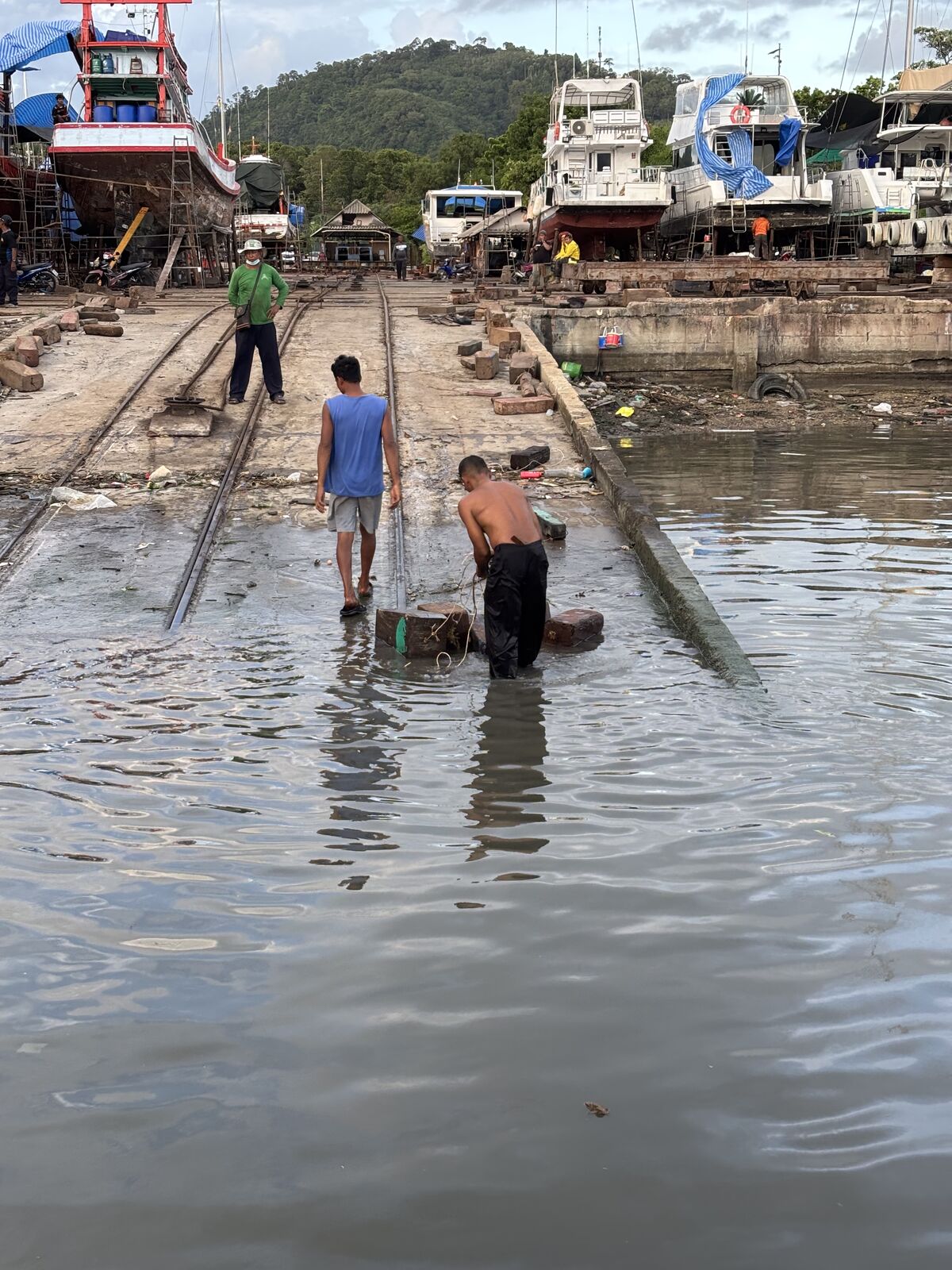 Crew wading through the slipway shallows at the boatyard, boats hauled out behind them