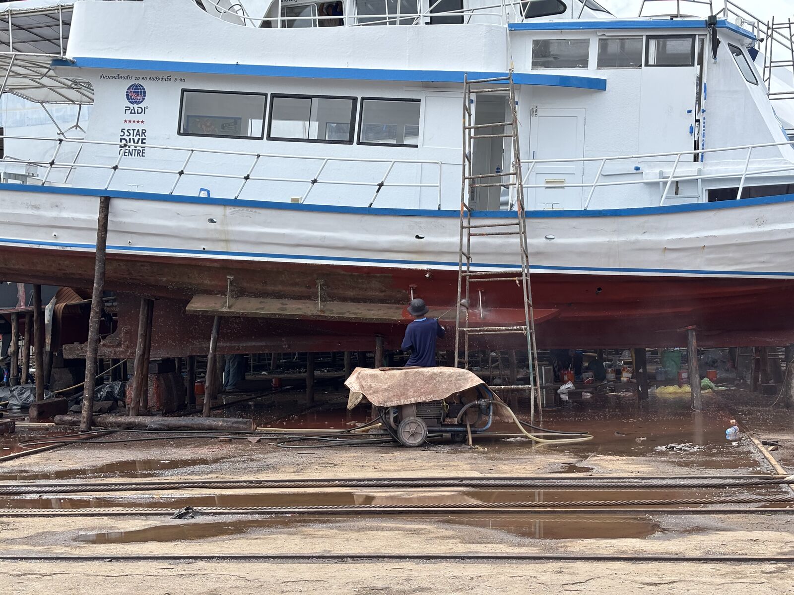MV Matchanu on the blocks, a ladder against her side and the hull sanded back below the blue stripe
