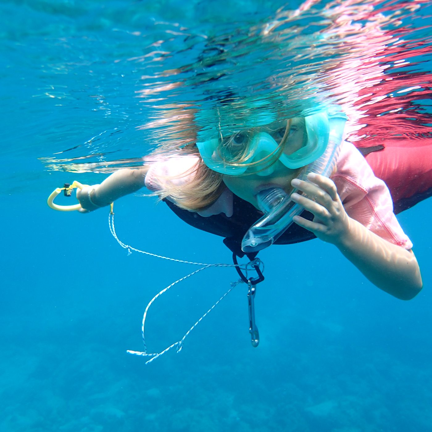 A snorkeller floating face down at the surface over pale sand and rock