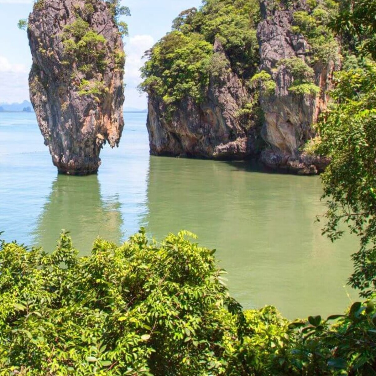 Tall limestone islets rising from a calm bay, viewed through green foliage