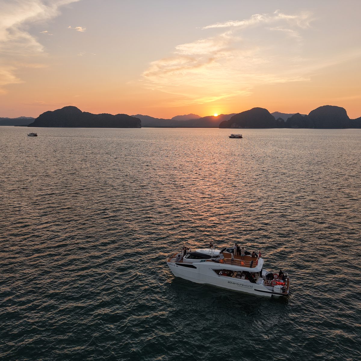 A white catamaran on calm water among limestone islands at sunset, seen from above