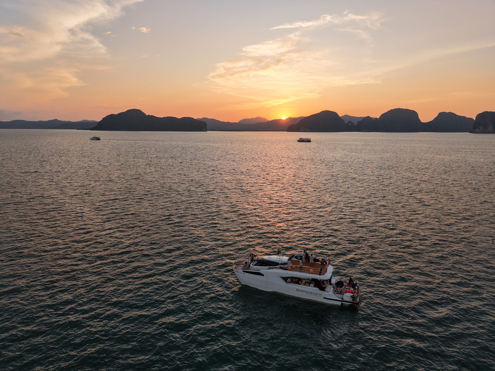A white catamaran on calm water among limestone islands at sunset, seen from above