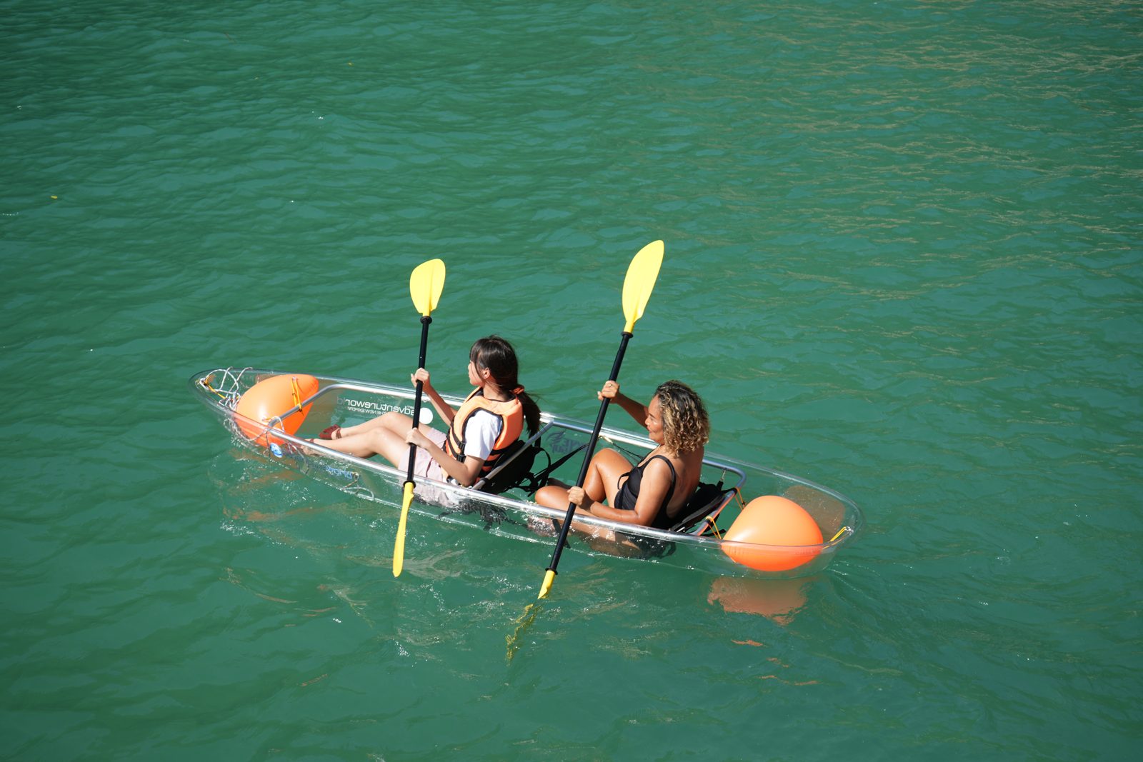 Two people in a clear kayak on flat green water