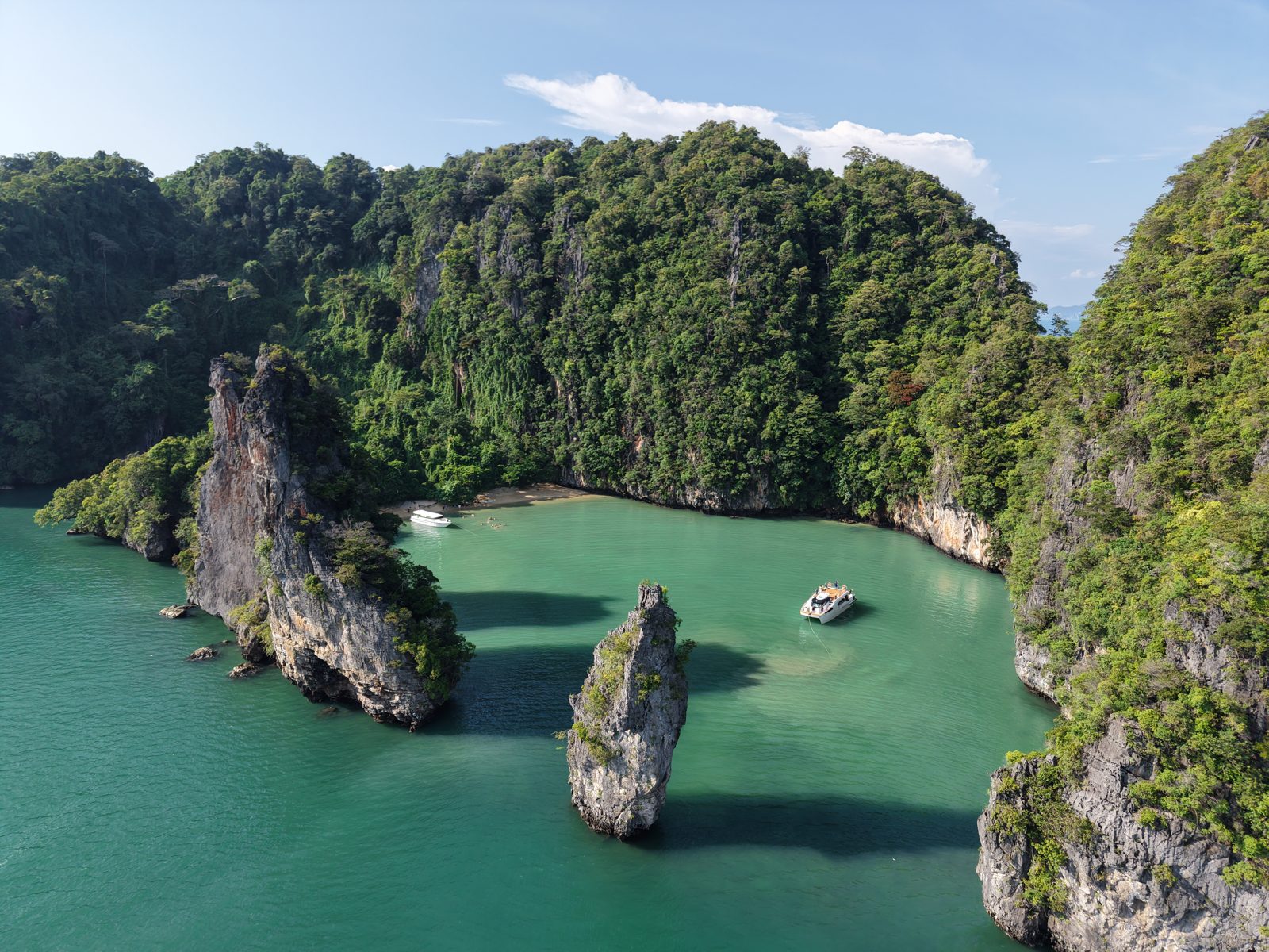 A green lagoon enclosed by limestone cliffs, a boat and a kayak inside it, seen from above