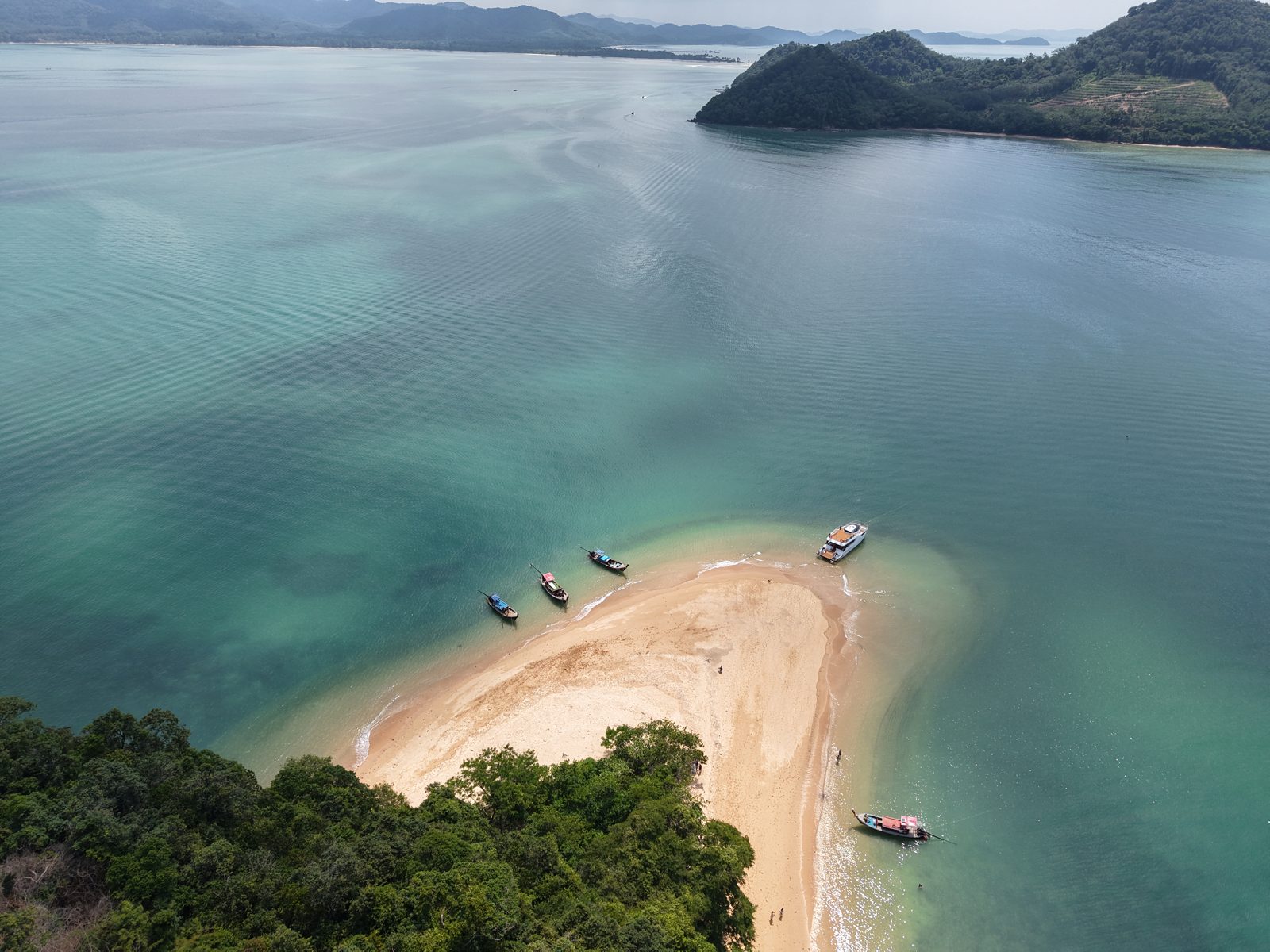 A pale sandbank curving between two islands, a boat anchored beside it