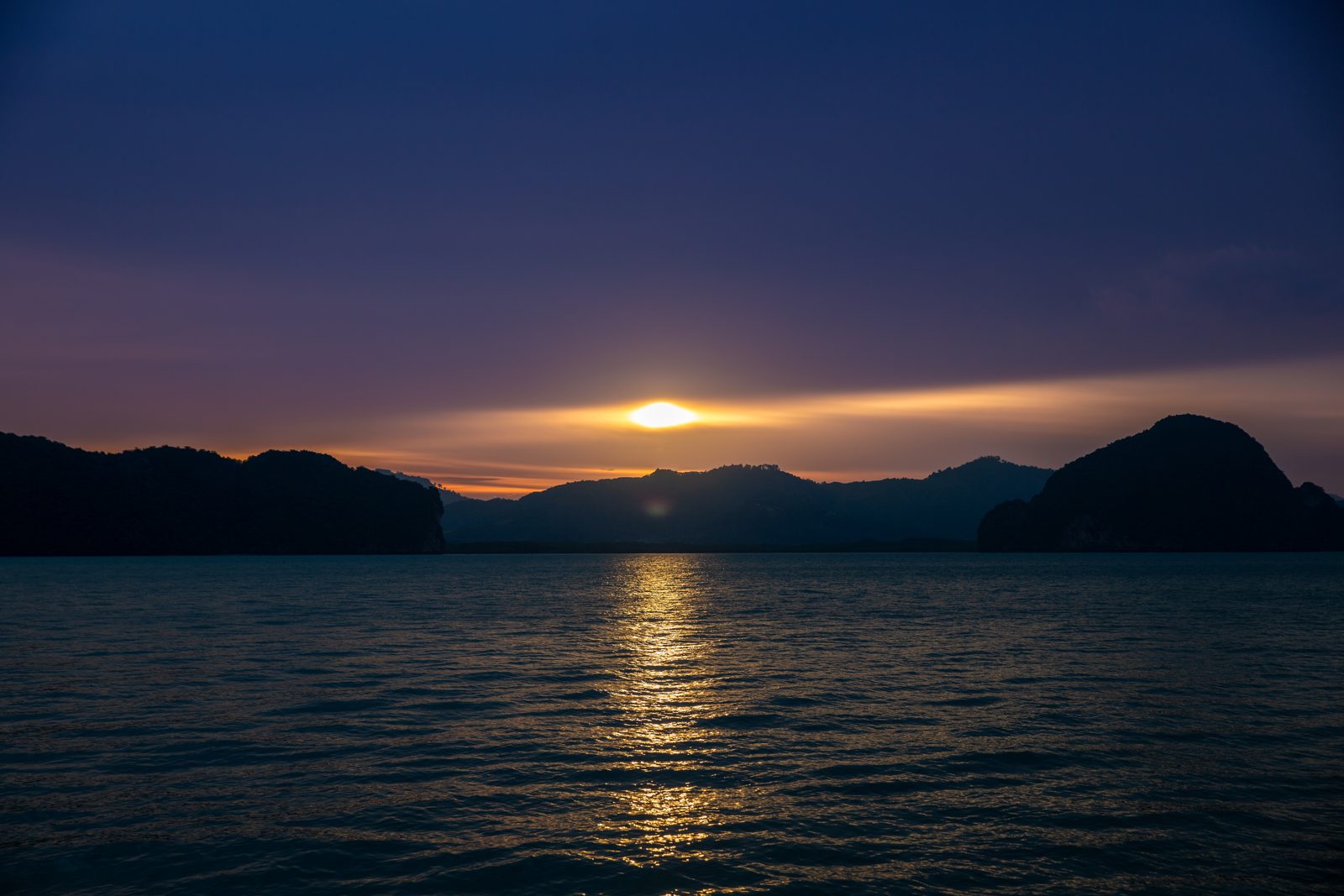 The sun setting behind islands, orange sky over dark water