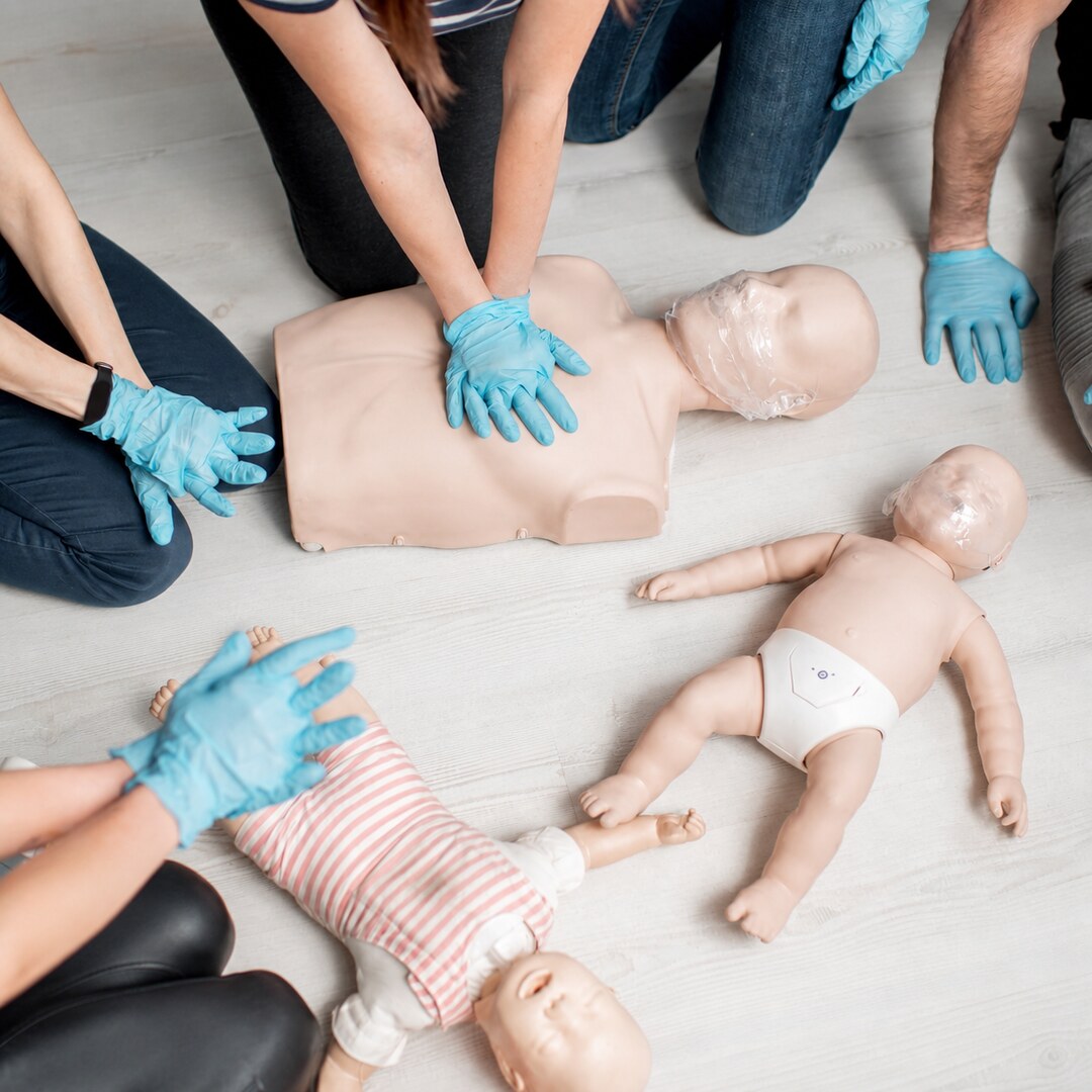 Gloved trainees practising compressions on adult and infant CPR manikins