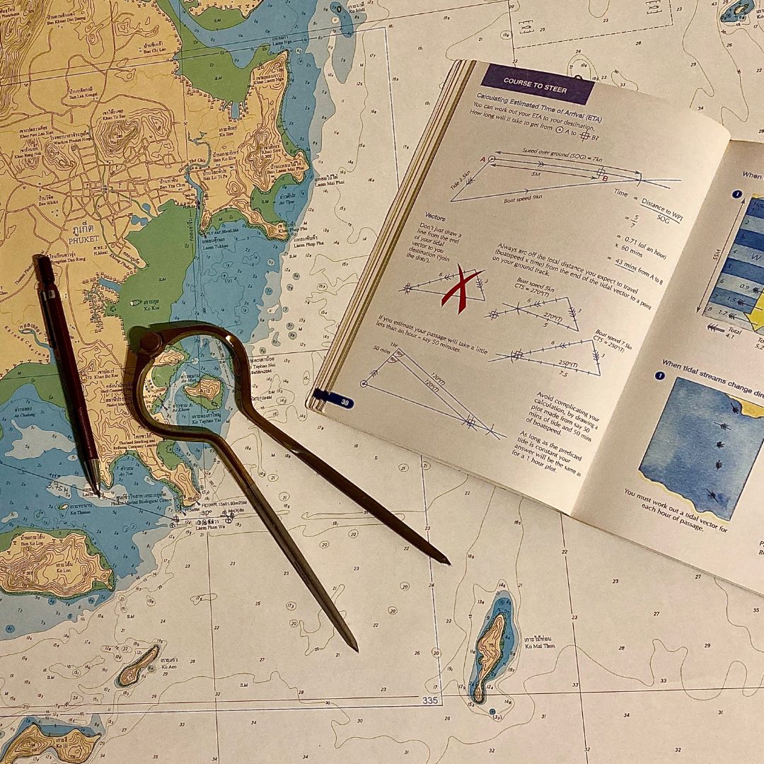 Navigation dividers and a course-to-steer booklet lying on a nautical chart of Phuket waters
