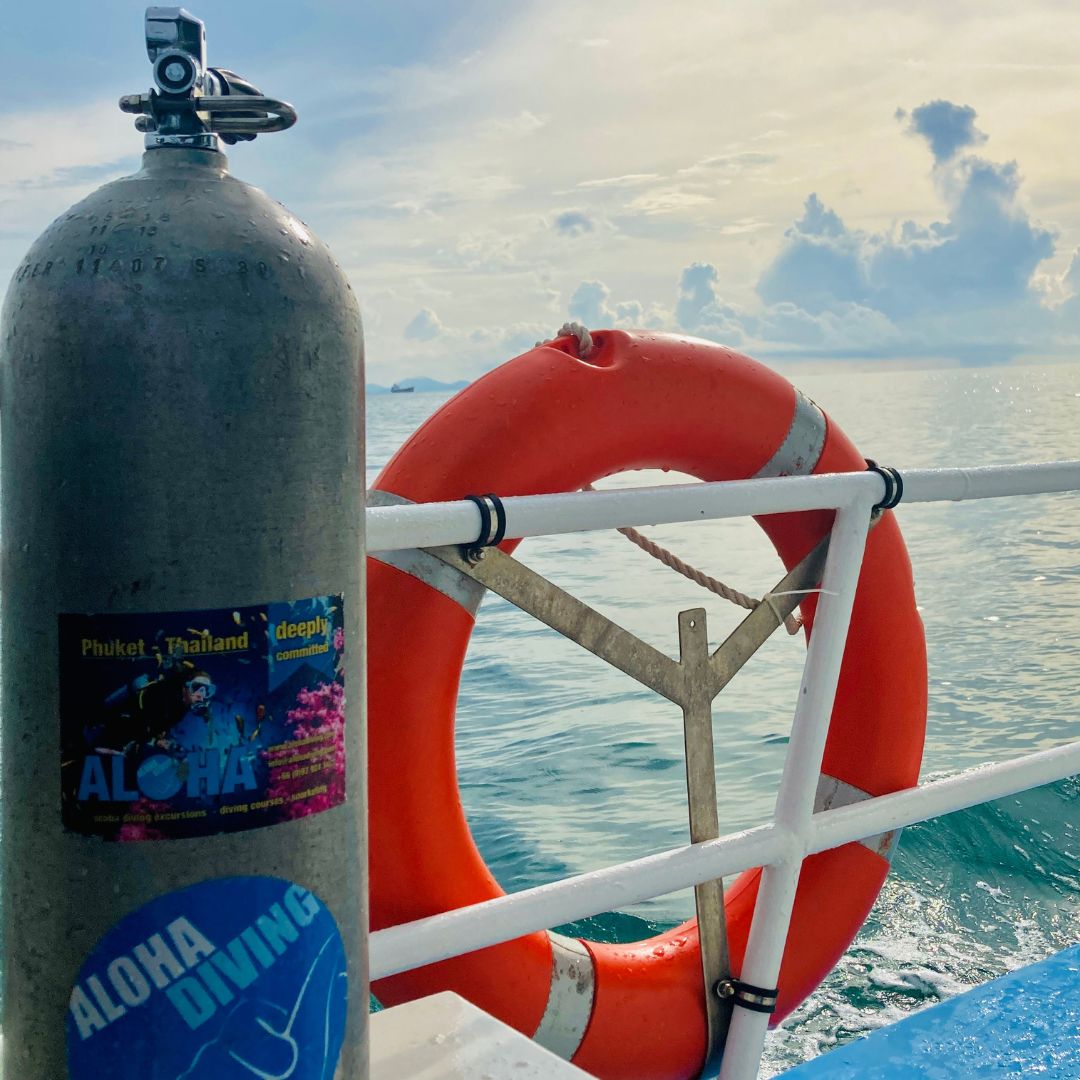 Scuba cylinder with Aloha Diving stickers beside an orange lifebuoy on a boat rail at sea